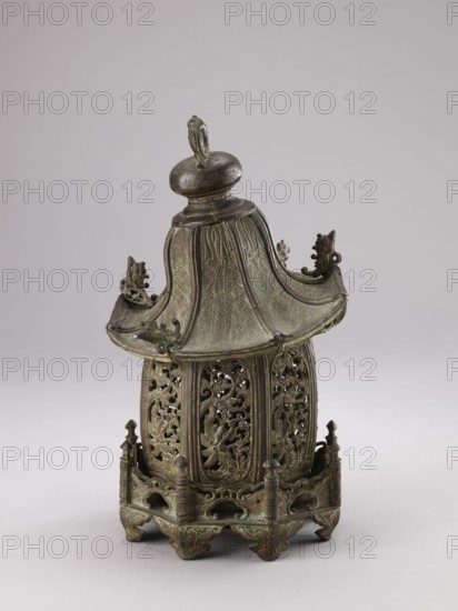 Lantern, gift; Chinese; Qing dynasty 1644–1911; 19th century; materials/technique: not specified; subject/decoration: fish, arbors, plants, garden arbors; height 35.0 cm., An ornate metal object sits against a pale gray background, showing a patinated greenish-brown surface with darker brown highlights; it has a pagoda-like roof with a rounded finial on top and gently upturned corners decorated with small sculpted figures, a flared midsection with textured panels, and a lower section of openwork panels featuring scrolling floral and foliate designs; the base is an elevated platform with carved supports and pierced arches, all sharing the same aged green and brown metal tones.