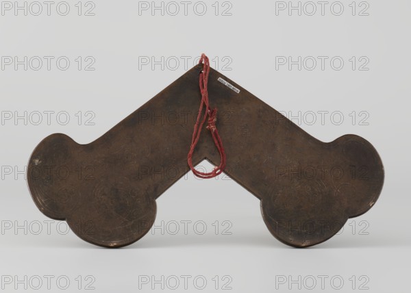 Gong, Chinese, Qing 1644–1911, 18th century, idiophone percussion instrument. Bronze gong with silver inlay, plant ornaments and tendrils, Chinese calligraphic inscriptions. Height 15.0 cm, width 28.0 cm., A dark brown, symmetrical object with rounded ends and a peaked center sits against a pale gray background, showing a worn, slightly reflective surface with faint decorative incised patterns; a loop of frayed red cord is threaded through a hole near the top peak and hangs down toward the center, and the object casts a soft shadow on the pale surface beneath it.