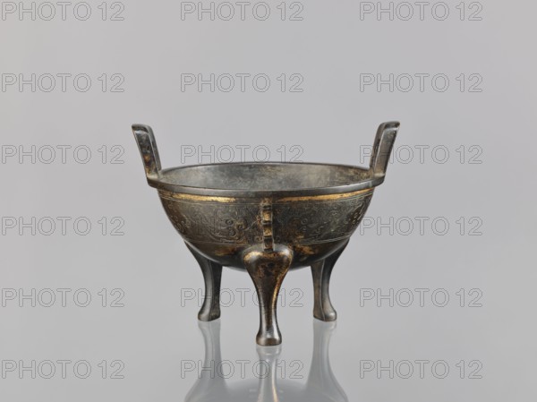 Ding incense burner, Chinese, beasts fantasy, meander ornament, leiwen ornament, Qing 1644–1911, ceremonial/ritual vessel, 19th century, China, vessel censer, height 12.6 cm, width 16 cm, diameter 14.5 cm, A small metal tripod vessel with a rounded bowl supported by three curved legs and two upright handles, showing decorative engraved patterns on the bowl; the metal surface is a mix of dark gray and aged bronze tones with areas of golden highlights and darker patina, and the vessel sits on a reflective pale gray surface against a soft light gray background.