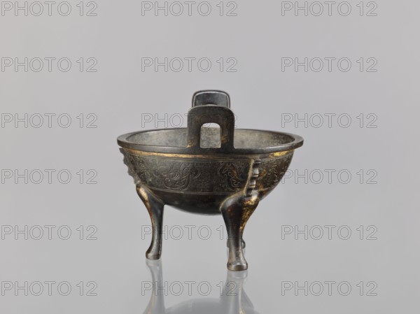 Ding incense burner, Chinese, Qing 1644–1911, 19th century, ceramic/bronze vessel censer; ritual/ceremonial vessel decorated with beast fantasy motifs, meander and leiwen ornament; height 12.6 cm, width 16 cm, diameter 14.5 cm., A small three-legged bronze vessel with a rounded bowl and a short pedestal handle rising from the rim sits on a reflective surface; the vessel shows a dark patina with areas of brownish-gold highlights and subtle greenish oxidation, and the bowl exterior is decorated with incised swirling and geometric patterns; the three legs curve outward and have smoother, shinier brown-gold wear at their outer faces, and the interior of the bowl appears darker and more matte; the background is a smooth, pale gray.