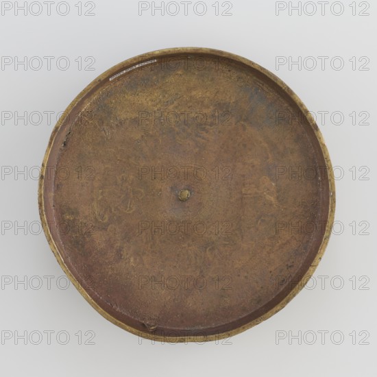 Cover; /author; craft; Tibetan culture; unknown provenance; symbols: eight preciousnesses ba bao carved symbols; square with pyramidal boss; 19th century; Mongolia and Tibet places of origin; varia; diameter 12.7 cm., A round shallow dish viewed from above with a raised rim, showing an aged, uneven surface in shades of brown, reddish-brown, and gold, with a slightly darker central spot and a small raised bump at the center; the rim appears metallic gold with areas of wear and darker mottling, and the interior surface shows subtle irregular patterns and texture in brown and rusty tones against a light gray background.