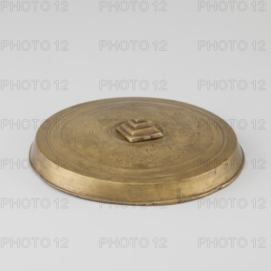 Cover; maker, hand-crafted; Tibetan; carved symbols of the Eight Preciousnesses ba bao; square with pyramidal boss; 19th century; Mongolia and Tibet places of origin; diameter 12.7 cm., A circular metal object with a low rim and a stepped square knob at its center, shown against a plain light background; the surface has engraved decorative motifs around the center and shows areas of wear; visible colors include shades of gold, brass, brown, and small darker discolorations.
