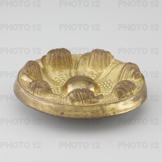 Seven-leaf rosette, crafted Tibetan, 19th century; materials and function: rosette ornament with seven leaves and decorative elements; provenance: Tibet, Mongolia; dimensions: height 4.3 cm, diameter 12.4 cm., A small round metal dish with a raised central dome and a petal-like arrangement of rounded protuberances around it, all rendered in a gold color with areas of darker, aged patina; the dish surface shows textured ridges and small bead-like details between the petals, and the rim appears slightly worn with visible scuffs in shades of gold and brown against a neutral light gray background.