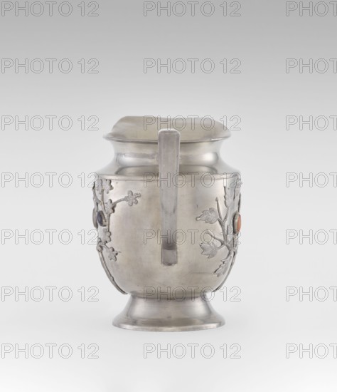 Jug, plant ornament, Chinese, Chinese art, teapot form, fruit ornament, applied plastic decoration: flowering, leafy bunches with oval set semi-precious stones, plum trees motif, Qing dynasty 1644–1911, 19th century, China; vessel, height 20.6 cm, width 23.0 cm., A metallic pitcher with a smooth, silvery surface sits against a pale gray background; it has a flared base, a rounded body, a slightly flared neck, and a square-edged handle running vertically down the front. A few raised floral and leaf decorations are attached to the sides of the body, and small round cabochon-like accents in dark and orange hues are set within the floral motifs. The overall colors visible are silver, gray, dark bluish, and orange.