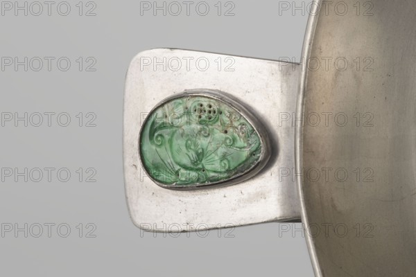 Vessel, Chinese, plant ornament and decorative motifs including Chinese symbols, Qing dynasty 1644–1911, 19th century, China; vessel; height 8.3 cm, diameter 20.0 cm, A close-up of a metallic object showing a rectangular silver-toned surface with rounded corners and a raised oval setting holding a green, carved stone with swirling, organic patterns, paired with a curved silver rim of a larger vessel visible at the right edge; colors present include silver, green, pale gray, and hints of darker gray and brown.