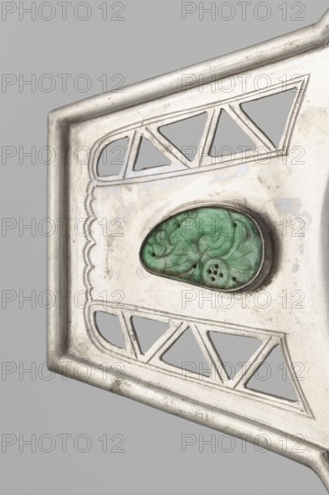 Platter, Chinese, Chinese art, openwork, bats iconography, coins, Qing 1644–1911, platter on a foot with two trapezoidal handles, 19th century, China, vessel; height 48.8 cm, width 24.0 cm, A close-up of a metallic object showing a section of a frame with a matte silver surface and a few areas of darker tarnish; the frame has cut-out triangular and rounded geometric shapes and a scalloped decorative groove along one edge, and set into the metal is an irregular oval green stone with carved floral patterns and subtle darker veining.