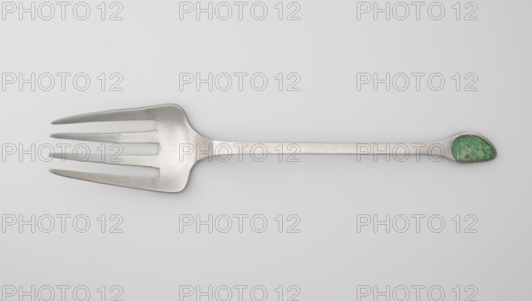 Serving fork; maker, Chinese; cutlery decorated with bats and coins; used in kitchens; Qing dynasty 1644–1911, 19th century; China; height 24.9 cm, width 4.9 cm, A metal serving fork with a long handle and a wide four-tined head lies horizontally against a pale gray background; the fork is silver-gray with a slightly brushed finish, and the rounded end of the handle contains a green stone-like inlay with mottled lighter and darker green tones.