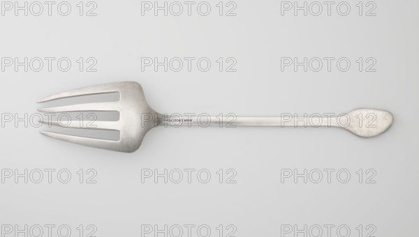 Serving fork; maker, Chinese; cutlery; coins and bats iconography; kitchens; Qing dynasty 1644–1911, 19th century; China; height 25.2 cm, width 5.0 cm., A metal serving fork lies horizontally against a light gray background, showing a matte silvery surface with subtle scratches and wear; the fork head on the left has a wide, flattened shape with four long, narrow tines and smooth rounded edges, while the long handle tapers toward a rounded, slightly flattened end on the right; overall colors visible are silvery gray and light gray, with faint darker gray shadows beneath the utensil.
