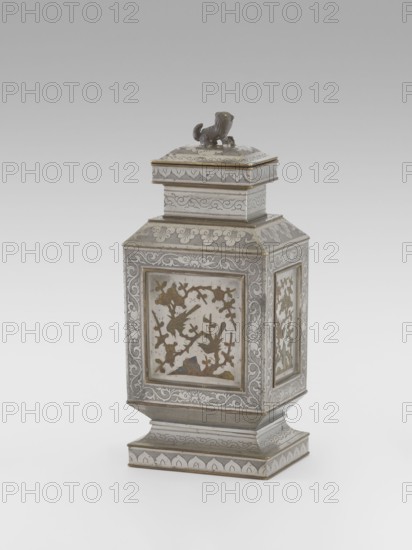 Teapot with a lid, tea, plums, birds, Chinese art, plant ornament, Chinese culture, restitution provenance, lions iconography, birds and flowers, huaniao style, fo iconography, plant twig, Qing style, clouds, Qing 1644–1911. Teapot with a profiled foot and neck, with a rectangular lid topped with a plastic figurine of a lion. Decorated with panels filled with a motif of a blossoming plum tree and birds, bordered with plant twigs the motif in the panels is engraved and set with metal. Foot, neck and cap decorated with plant ornament powdered background. 19th century, China, vessel, height 27.3 cm, width 11.5 cm, depth 8.3 cm., An ornate metal container with a square base and stepped pedestal rising to a rectangular body topped by a stacked, lidded section and a small sculpted animal finial; the surface shows intricate engraved and inlaid decorative patterns with floral and scrolling motifs, framed panels on the sides containing cutout shapes arranged as a scene of birds among branches, ...