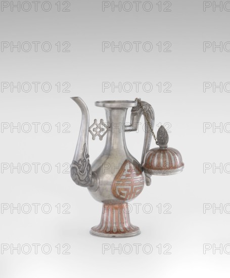 Wine jug, Chinese, plastic decorations of lotuses, longevity shou character, and dragons; Qing 1644–1911, early 20th century, China; vessel; height 26.8 cm, width 17.5 cm., A metal ewer with a rounded body, flared neck, and pedestal base sits against a plain light gray background; the vessel is primarily silver with areas of reddish-brown decoration on the body, base, and attached domed lid. The ewer has a long curved spout with embossed ornament near its base and a decorative handle with a chain connecting to the lid; a few geometric openwork elements project from the neck area. The pedestal base shows vertical fluting highlighted in reddish-brown, and the domed lid has alternating silver and reddish-brown ribs with a sculpted finial on top. The surface of the metal shows a smooth, slightly reflective finish with sculptural detailing on the spout, handle, and finial.