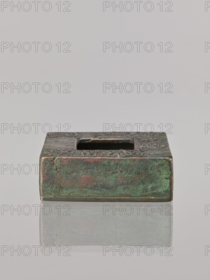 Water container, Narozno Eckersdorf; Chinese art; Chinese culture; inscriptions Chinese; Qing 1644–1911, 19th/20th century; China; vessel; height 2.6 cm, width 7.5 cm, depth 7.4 cm., A low, rectangular metal object with a square hole in its top surface sits on a reflective surface; the metal shows a weathered patina with shades of green and turquoise, areas of reddish-brown and brown, and darker grayish tones, and the top edge displays some textured, uneven markings.