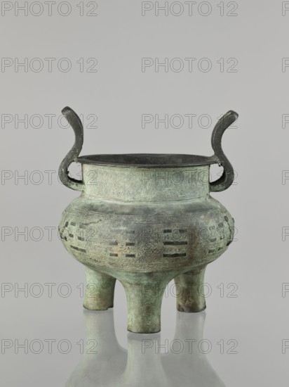 Ding-type incense burner, maker, purchase, Chinese; Qing dynasty 1644–1911, 17th–18th century . Bronze vessel with geometric ornament; associated with ceremonial use, Chinese philosophy and fortune-telling. Height 23 cm; width 19.4 cm; diameter 18.7 cm., A metal vessel with a greenish patina stands on a reflective surface; it has a rounded body tapering to a narrower neck, a flared rim, and two upward-curving handles on opposite sides. The body rests on a group of short, sturdy legs and displays a pattern of incised geometric motifs and rectangular cutouts around its midsection. The metal shows areas of darker and lighter green along with hints of brown and gray, and the interior rim appears darker than the exterior. The background is a smooth, light gray.