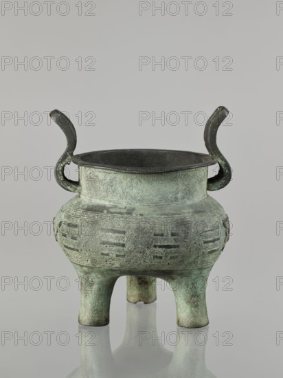 Ding-type incense burner, maker, Chinese; Qing 1644–1911, 17th–18th century ; vessel; ceremonial use; geometric ornament; associated with philosophy and fortune telling; height 23 cm, width 19.4 cm, diameter 18.7 cm., A greenish metal vessel with a patina finish stands on a reflective surface, featuring a rounded body and three short legs; the vessel has a wide rim and two upward-curving handles that are darker in color, and the body is decorated with textured geometric patterns and bands of slightly different green and darker tones.