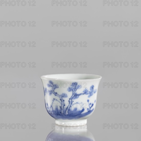 Bowl, 18th century Japan, Japanese ceramics, blue and white porcelain; vessel with painted scene of fishermen and figures in a landscape. Height 3.8 cm; width 5.0 cm., A small white porcelain cup with a flared rim sits on a reflective surface; it has a blue painted design of tree-like branches and foliage wrapping around the exterior, with a concentrated blue wash near the base and delicate blue brushwork forming leaves and stems; the background is plain light gray and the reflection of the cup on the surface shows muted white and blue tones.