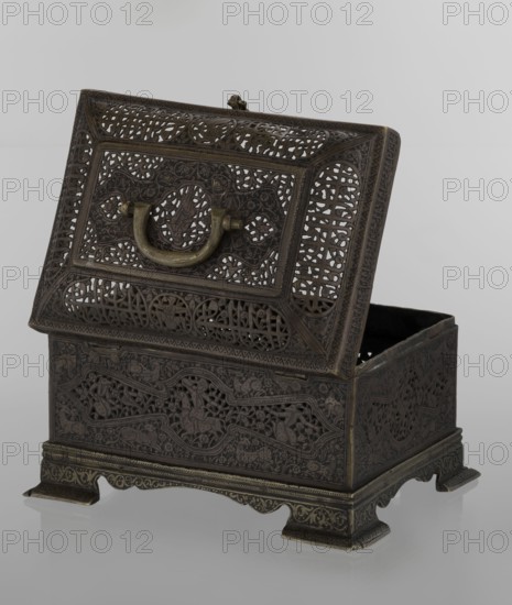 Box; Persian Qajar dynasty, 19th century. Rectangular box on four feet with a lid and handle. Iran. Decoration includes animals, hares, fantasy figures, hunting scenes with archers, figurative motifs, inscriptions, handles. Height 19.9 cm; width 15.6 cm; depth 13.8 cm., An ornate metal box with a hinged lid shown partially open, featuring intricate openwork panels and carved decorative patterns across its surfaces; a curved metal handle with a slightly different metallic tone is mounted on the front of the lid; the box stands on a raised scalloped base with small feet and detailed border motifs; visible colors include dark brown and brassy gold tones, with a neutral pale gray background and a faint reflective surface beneath the box.