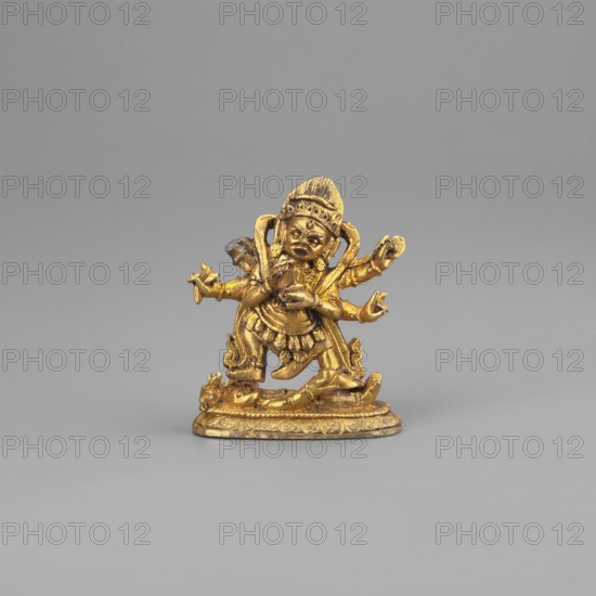 Six-armed Mahakala, unknown sculptor, Himalayan Tibetan Buddhist dharmapala figure, on base, 2nd half of the 19th century, Mongolia; sculpture, figurine; height 3.8 cm, width 3.1 cm, A small golden figurine stands on an oval base against a plain light gray background; the figure has a rounded headpiece and a detailed face with pronounced features, multiple arms extended in different directions, and ornate clothing with layered skirts and decorative elements; the base and figure show textured patterns and sculpted details, and the visible colors are gold and light gray.
