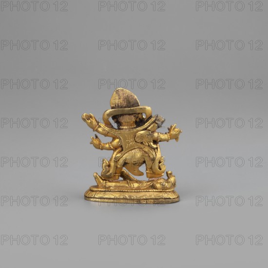 Six-armed Mahakala, unknown sculptor, 2nd half of the 19th century, Tibetan Buddhist Himalayan art; dharmapala iconography; Mongolia place of origin; sculpture, figurine; height 3.8 cm, width 3.1 cm, A small gold-colored metal figurine stands on a flat decorative base against a plain light gray background; the figurine shows a rounded head with a hat-like top, a curved collar or halo behind the head, a torso with sculpted folds and ornamentation, multiple outstretched arms with open hands, and stylized lower limbs and flowing drapery details. The visible colors are gold on the figurine and light gray in the background.