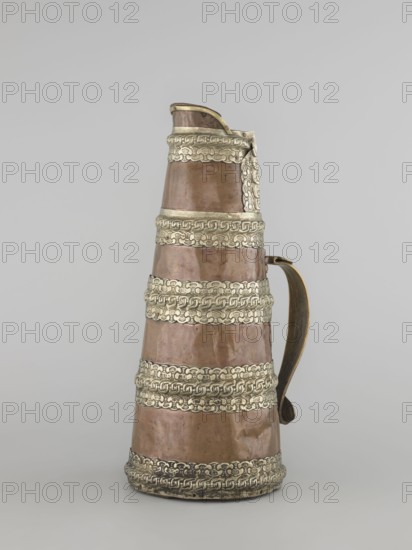 Tea pot;, 19th century, Tibet. Tea vessel/jug tapering towards the top with silver fittings and brass handle. Height 35.0 cm; width 19.0 cm; diameter 15.0 cm., A tall conical metal pitcher with a curved handle stands against a plain pale gray background; the body of the vessel is copper-colored with a warm reddish-brown tone and it is divided into several tapered sections by ornate bands of a pale silvery metal that feature a repeating linked pattern, the handle is darker bronze with a slightly greenish patina near the edges, the spout area at the top is edged in the same pale silvery metal and the surface of the copper shows subtle dents and variations in sheen.