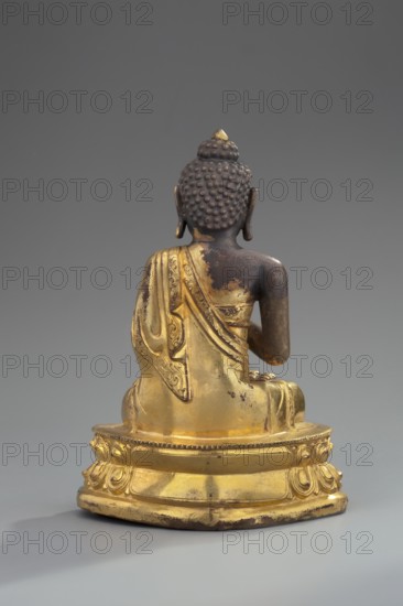 Shakyamuni Buddha, unknown sculptor, Himalayan culture, Sino-Tibetan style, Himalayan/Tibetan Buddhist art; Buddha ca. 560–480 BCE, iconography: ushnisha, lotus throne, mudras; 18th century, Tibet; sculpture, figurine; height 11 cm, width 7.7 cm, A gilded seated statue shown from behind on a rounded ornate base, with a dark brown head and shoulders featuring textured hair curls and elongated ears, and a golden robe draped over one shoulder with visible decorative patterns and worn areas; the base and lower garment are gold with some darker worn spots, and the background is a smooth neutral gray.