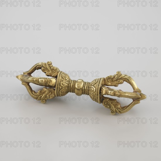 Vajra; maker, 19th century; Tibet; Tibetan Buddhist ritual object vajra; Buddhist art; craft; ritual use; height 9.6 cm, width 3.0 cm., A metallic object with an aged golden color sits on a pale gray surface against a light gray background; it has a symmetrical, elongated form with an ornate central bulbous section featuring textured bands and rounded protrusions, and each end flares into an open, curved trident-like shape decorated with scrollwork and leaf-like motifs, the whole piece showing a warm yellow-gold patina with darker recessed areas and subtle highlights.