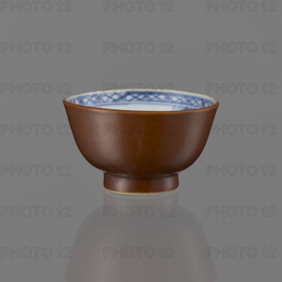 Alcohol bowl, Chinese, Qing 1644–1911, 19th century, blue-and-white porcelain vessel with landscape motifs; height 4.5 cm, diameter 7.8 cm., A small bowl with a smooth reddish-brown exterior and a white interior rim decorated with a patterned band in blue sits on a reflective gray surface against a uniform gray background, showing a soft reflection beneath it.