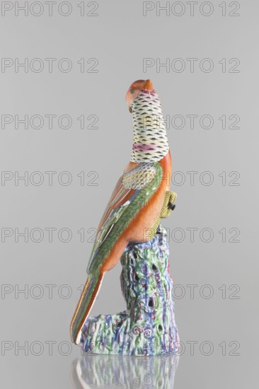 Pheasant figurine, Chinese, Qing dynasty 1644–1911, 19th century. Colored porcelain sculpture of a pheasant perched on rocks; height 49.0 cm, width 20.0 cm. Materials: ceramics; subject: animal figurine/bird., A colorful ceramic bird perched on a textured, multicolored base, shown in profile against a plain light gray background; the bird has an orange body, a white neck patterned with black marks and faint pink and yellow accents, green wings with layered feather detailing in shades of green, blue, and gold, and a long tail featuring orange and green with gold striping; the base displays a marbled mix of green, blue, purple, and pink with a glossy finish and the scene includes the bird's yellow foot gripping the base.