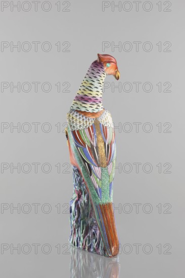 Pheasant figurine, Chinese, Qing 1644–1911, 19th century; ceramics, colored porcelain; subject: pheasant and rocks; sculpture; height 49.5 cm, width 19.8 cm, depth 17.0 cm, weight 3.36 kg; animal figurine bird., A colorful bird sculpture perched on a textured base is shown from the back and side against a plain light gray background, featuring a red head with an orange beak and a turquoise eye, a neck and upper back with pastel shades of pink, yellow, green and black feather patterns, wings decorated with vivid sections of red, blue, green, purple, pink, black and gold, and a long tail with orange and blue stripes; the base below the bird displays marbled swirls of purple, green and blue, and the surface beneath reflects the sculpture.