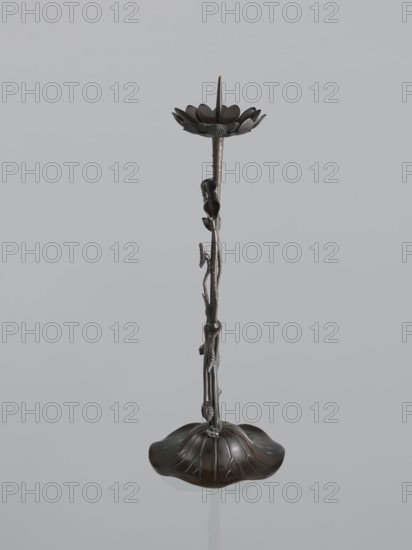 Candlestick shokudai, Takimoto craftsman, Japanese, lotuses and leaves motif, Meiji period 1868–1912, 2nd half of the 19th century, Japan; candlestick; height 46.0 cm; provenance unknown., A tall, slender metal object with a dark brown and black finish shaped like a plant stem rising from a wide, curved base resembling a large leaf, the stem featuring a few sculpted buds and small leaves along its length, topped by a flower-like cup with layered petal shapes and a central pointed spike; colors visible include dark brown, black, and hints of bronze against a pale grey background.