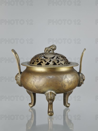 Ding-type incense burner with cover, Chinese, ceremonial vessel censer, bronze, engraved plant ornament on sides of burner and cover; decorated with plum trees, bats, lions, fo, hares, bamboos, pine trees, deer, cranes, rabbits and yin-yang motifs; Qing dynasty 1644–1911, 18th–19th century, height 27.0 cm., An ornate metal vessel with a warm golden-brown patina sits on a reflective surface, featuring a rounded body with engraved decorative patterns and a domed pierced lid topped by a small sculpted animal figure; the vessel stands on three curved legs ending in stylized heads and has two upward-curving handles with sculpted mounts on either side, showing colors of gold, brass, and subtle darker brown areas against a pale gray background.