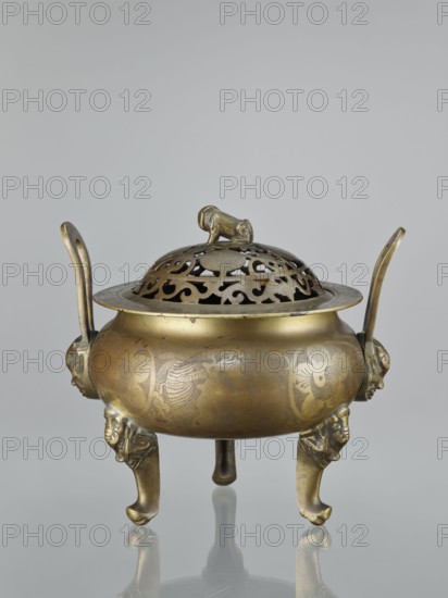 Ding-type incense burner with cover, Chinese, ceremonial vessel, ding-type censer, engraved plant ornament on sides of burner and cover, decorations: plum trees, bats, lions fo, hares/rabbits, bamboos, pine trees, deer, cranes, yin and yang motifs, Qing dynasty 1644–1911, 18th–19th century, China, height 27.0 cm, A metal incense burner with a round body and a pierced domed lid topped by a small sculpted animal figure sits on a reflective surface; the burner has a warm gold and brass tone with darker patina in places, two upward-curving handles, decorative engraved floral and patterned motifs on the bowl, and three short legs each ending in stylized animal-head forms, with the overall palette showing shades of gold, brass, and darker brownish areas.