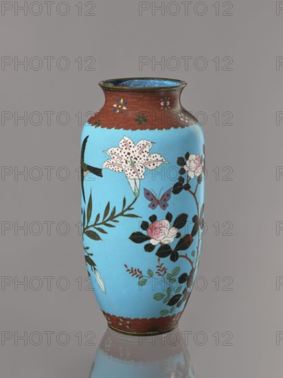 Vase, Cloisonné enamel on copper with brass rims at the spout and foot. Short, slightly flared neck. Decoration on a blue background: large motifs of rose bushes and lilies, small flowers, two butterflies and a bird. Iconography: flowers, butterflies, roses, lilies, birds kachôga. Japanese, Meiji period, ca. 1905–1908. Vessel; height 30.7 cm, diameter 10.6 cm., A tall vase with a rounded body and slightly flared rim sits against a plain background; the vase is primarily bright blue with decorative bands of reddish-brown at the top and bottom, and features painted floral motifs including a large spotted white lily, pink rose-like flowers, dark green leaves, a small purple butterfly, and other leafy sprigs in shades of green and red, with areas of black used for stems and leaf accents and a thin metallic rim at the mouth.