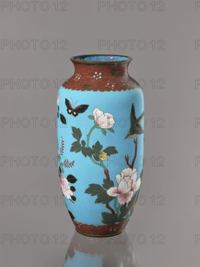 Vase, Cloisonné enamel on copper with brass rims at the spout and foot. Short, slightly flared neck. Decoration on a blue background: large motifs of rose bushes and lilies, small flowers, two butterflies and a bird; iconography includes flowers, butterflies, roses, lilies, birds kachôga. Meiji period, ca. 1905–1908. Japan. Vessel. Height 30.7 cm; diameter 10.6 cm., A tall vase with a narrow neck and rounded body sits against a neutral gray background; the main surface is bright turquoise blue decorated with floral branches bearing pale pink and white blossoms and dark green leaves, a few thin reddish-brown branches, and a black and yellow butterfly and a green bird in flight; the rim and base borders are a textured reddish-brown with small floral motifs, and the interior near the rim shows a darker blue.