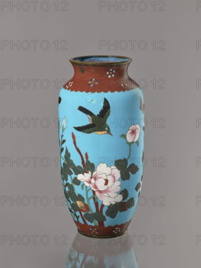 Vase, Cloisonné enamel on copper with brass rims at the spout and foot. Decoration: large roses and lilies, small flowers, two birds and a butterfly on a blue background kachôga. Short, slightly flared neck. Japanese, Meiji period ca. 1905–1908. Vessel. Height 30.8 cm; diameter 10.6 cm., A tall vase with a glossy sky-blue body and a narrow neck rimmed in a reddish-brown band decorated with small floral motifs, featuring a painted scene of a green and black bird in flight above a cluster of dark green leaves and pale pink peony-like blossoms with reddish stems; the interior of the rim shows a darker bluish tone, and the base edge repeats the reddish-brown band with small floral accents, all shown against a neutral gray background with a subtle reflection beneath the vase.