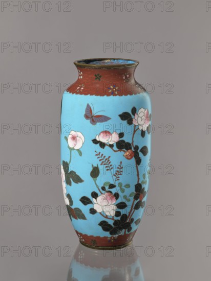 Vase. Cloisonné enamel on copper with brass rims at the spout and foot. Short, slightly flared neck. Decoration: large roses and lilies, small flowers, two birds and a butterfly on a blue background kachôga. Japanese, Meiji period, ca. 1905–1908. Height 30.8 cm; diameter 10.6 cm., A tall vase with a bright sky blue body and dark reddish-brown rim and base, decorated with painted floral branches bearing pale pink and white blossoms and dark green leaves, a few buds, and a single purple and red butterfly near the upper area, all set against a neutral gray background with a subtle reflection of the vase at the bottom.