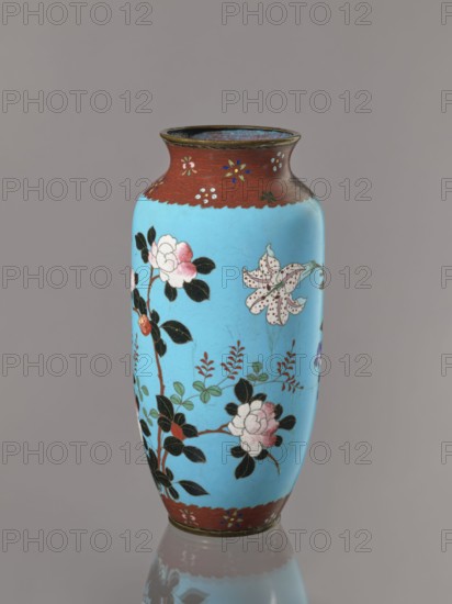 Vase. Cloisonné enamel on copper with brass rims at the spout and foot. Short, slightly flared neck. Decoration: large roses and lilies, small flowers, two birds and a butterfly on a blue background kachôga. Japanese, Meiji period, ca. 1905–1908. Height 30.8 cm; diameter 10.6 cm., A tall vase with a rounded shoulder and flared rim stands against a plain background, predominantly light blue in color with a band of reddish-brown around the rim and base; the blue surface is decorated with floral motifs including white and pink blossoms with dark green and black leaves, stems in brown, and additional small leafy sprigs in green and reddish-brown, while the reddish-brown bands feature small stylized flower accents in blue, white, yellow, and green.