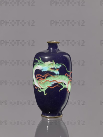 Vase, cloisonné enamel on silver, Meiji period 19th/20th century, Japan. Vase on a low ring-shaped foot with a short thin neck slightly flared at the spout. Decoration features dragons Japanese iconography. Height 11.8 cm; diameter 6.1 cm., A dark blue glossy vase with a narrow neck and rounded body stands against a neutral gray background; its surface shows a decorative dragon motif in shades of green with pale blue accents and red-orange flowing ribbons, and the vase has gold-colored trim at the rim and base with a subtle reflection visible beneath it.