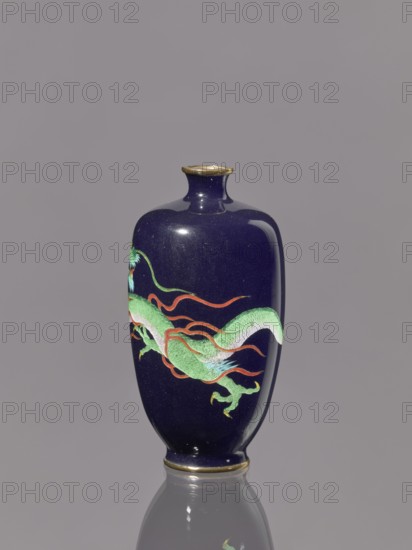 Vase, Meiji period 1868–1912, late 19th/early 20th century, Japan. Cloisonné enamel on silver. Vase on a low, ring-shaped foot with a short, thin neck slightly flared at the spout; decorated with cloisonné enamel featuring dragons. Vessel. Height 11.8 cm; diameter 6.1 cm., A dark navy-blue vase with a rounded body, narrow neck, and small flared rim sits upright on a reflective surface, showing its reflection beneath. The vase features a painted sinuous dragon motif in shades of green with lighter green scales and aqua highlights, accented by flowing red-orange ribbons and small yellow details on the dragon's claws. The rim and base edges have a thin metallic-gold band. The background is a uniform muted gray.