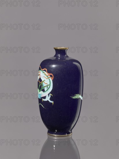 Vase, repossession Krakow — ; dragons iconography; Japanese art; Japanese dragon motif; Meiji 1868–1912; cloisonné enamel on silver. Vase on a low ring-shaped foot with a short thin neck, slightly flared at the spout. 19th/20th century Meiji Period, Japan. Vessel. Height 11.8 cm, diameter 6.1 cm., A dark blue glossy vase with a narrow neck and flared rim sits centered against a neutral gray background, showing a reflected base beneath it; the vase has a painted decorative motif in shades of light blue, green, white, orange, and yellow on one side, with a small extension of similar colors on the opposite side, and a thin gold-colored band around the rim and base.