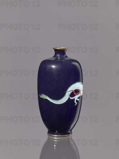 Vase, cloisonné enamel on silver; Meiji period 19th/20th century, 1868–1912, Japan. Vase on a low ring-shaped foot with a short thin neck slightly flared at the spout; decorated with cloisonné enamel featuring dragons/Japanese dragon motif. Vessel; height 11.8 cm, diameter 6.1 cm., A glossy vase with a deep navy blue surface and subtle speckling stands upright against a neutral gray background, featuring a painted serpentine creature in shades of pale green, mint, white, red, and orange wrapping around one side; the vase has a narrow neck with a small flared rim accented in a metallic gold color and a matching gold-colored base rim, and its reflection is visible on the shiny surface beneath it.