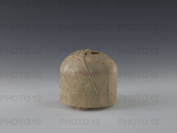 Tin with lid; maker, gift; Qing dynasty 1644–1911; 19th century; China; yurt decoration; container; height 12.8 cm; diameter 13.1 cm., A small rounded object sits on a smooth surface against a gradient background, appearing dome-like with a flat lower band and a slightly raised base; its surface shows a mottled mix of tan, beige, brown, and hints of green with areas of darker and lighter mottling, and there are carved or raised linear ridges and curved seams on the dome that create segmented panels and a small opening at the top.