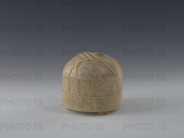 Tin with lid, gift, repossession, Chinese art, Chinese culture, Qing 1644–1911, yurts, 19th century, China, container, height 12.8 cm, diameter 13.1 cm, A small rounded object sits on a smooth surface against a gradient gray background, appearing as a domed container with a cylindrical base and short feet; its surface shows mottled shades of brown, tan, beige, and hints of green with weathered spots and subtle darker streaks, and there are raised curved lines forming a decorative pattern on the dome and a horizontal band around the base.