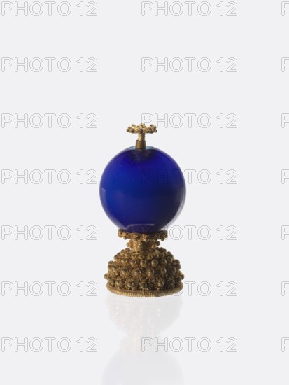 Button for a semi-official cap of a fourth-ranking official, gift, Chinese art, Chinese culture, Qing 1644–1911, officials, emblems. Button composed of a blue-navy glass ball mounted on a pin with a dome decorated with rosettes. 19th century, China. Jewelry, clothing; height 6.6 cm, diameter 3.1 cm., A decorative object consisting of a deep blue spherical element mounted on an ornate gold-toned base, topped with a small gold-toned floral knob; the blue sphere is smooth and glossy, the base is richly textured with clustered bead- and flower-like details, and the surfaces show reflections on the white background with visible colors of blue and gold.