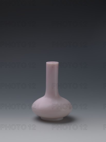 Vase, Chinese, Qing dynasty Qianlong, 1736–1795. Flask of pale pink glass on a low ring foot with a straight long cylindrical neck. 1736–1795. China. Vessel. Height 13.6 cm; diameter 9.8 cm; weight 0.35 kg., A small, rounded vase with a narrow, elongated neck and a bulbous base sits centered against a smooth gradient background; the vase is a pale pink color with subtle glossy reflections, and the background transitions from dark gray at the top to a lighter gray near the bottom, with a soft shadow beneath the vase.