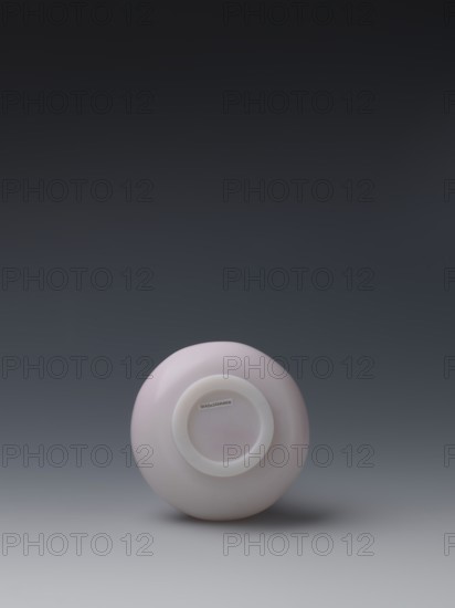 Vase, unknown creator; glass flask of pale pink glass on a low ring foot with a straight long cylindrical neck; Chinese, Qing dynasty, Qianlong period 1736–1795; vessel; height 13.6 cm, diameter 9.8 cm, weight 0.35 kg., A smooth round object sits centered near the bottom of the image, showing its underside with a recessed circular base; the object is pale pink with a slightly lighter circular rim at its center and casts a soft shadow on the surface beneath it, while the background transitions from a muted gray at the bottom to a darker gray-black toward the top.