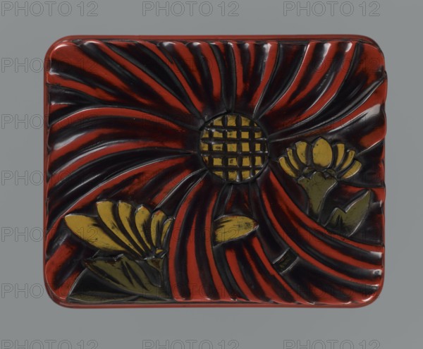Box with a lid., Japanese, Meiji period 1868–1912, early 20th century. Lacquer chôshitsu, carved; black, red, brown, yellow lacquer with carved flowers—chrysanthemums—and leaves. Rounded corners and a slightly distinct wavy-cut base. Container. Height 6.1 cm; width 14.0 cm; depth 10.8 cm; weight 208 g., A rectangular lacquered box with rounded corners sits against a plain gray background, its top carved with a large stylized flower design; a central circular element features a grid-like texture and is surrounded by sweeping curved petals that alternate in darker and lighter tones, and there are a few smaller flower shapes and leaves integrated into the composition. The visible colors include deep red, black, mustard yellow, and olive green, with highlights and shadows giving the carved surface a glossy appearance.