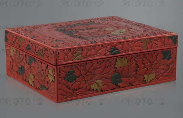 Box with a lid, Chinese art, Chinese culture, figural scenes, floral motifs, Qing 1644–1911, peonies, bamboos, geometric ornament, gourds, sages, scholars, fans, men. Decoration: on the lid a large reserve with a figural scene in a landscape; the rest of the background and sides with floral motifs. Red, black, green, and yellow lacquer, carved. 19th century, China. Container. Height 13.0 cm; width 36.5 cm; depth 28.5 cm., A rectangular decorative box sits on a reflective surface, covered in carved floral relief. The box is predominantly red with accents of dark green and muted yellow on the carved leaves and petals. The lid and sides show dense, overlapping flower and leaf motifs with textured, raised carving and smooth recessed background. The edges and corners of the box are finished in the same red, and the reflection below shows a softened mirror image of the box and its colors. The background behind the box is a flat neutral gray.