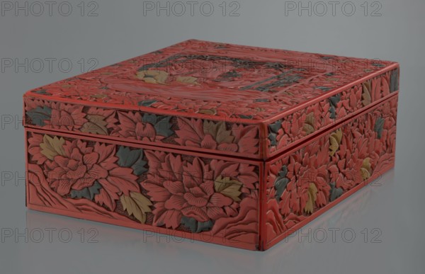 Box with a lid, Chinese art, Chinese culture, figural scenes, floral motifs, Qing 1644–1911, peonies, bamboos, geometric ornament, gourds, sages, scholars, fans, men. Decoration: on the lid a large reserve with a figural scene in a landscape; the rest of the background and sides with floral motifs. Red, black, green, and yellow lacquer, carved. 19th century, China. Container. Height 13.0 cm, width 36.5 cm, depth 28.5 cm., A rectangular carved box with a lid is shown against a neutral gray background and reflective surface; the box is covered in dense floral carvings with layered petals and leaves, with a dominant red color and accents of green and yellow on the carved foliage, and darker recessed areas that create shadowed texture across the top and sides.