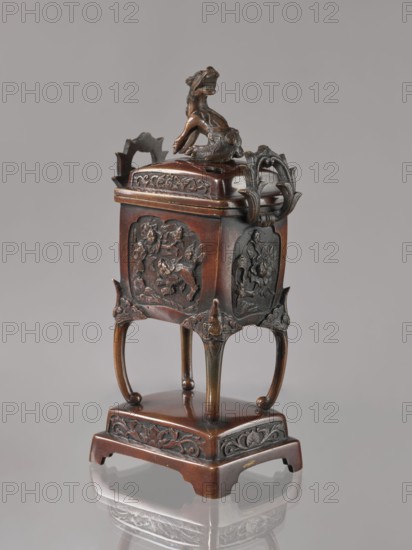 Incense burner kôro with cover, Japanese, Meiji 1868–1912. Bronze incense burner in the shape of a cuboid box on four slightly arched legs standing on a tall rectangular base. Panels with relief decoration of karashishi and peonies. Cover with four holes topped with a qilin. 2nd half of the 19th century. Vessel. Height 22.0 cm; width 9.5 cm; depth 7.5 cm., A small ornate container made of dark brown material with patinated darker accents stands on a square base; the base has carved floral motifs and curved cutaway corners, and it supports four slender legs that rise to a slightly larger square body with raised decorative panels showing low-relief sculpted scenes. The lid is topped by a sculpted mythical animal figure in a similar dark brown tone, and there are carved looped handles and ornamental corner elements with darker highlights. The overall colors visible are various shades of brown with darker brown or nearly black details, and the object sits on a reflective neutral surface ag...