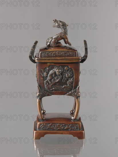 Incense burner kôro with cover, Japanese, Meiji 1868–1912. Incense burner in the shape of a cuboid box on four slightly arched legs standing on a tall rectangular base. Panels with relief decoration of karashishi and peonies. Cover with four holes topped with a qilin. Bronze vessel, 2nd half of the 19th century. Height 22.0 cm; width 9.5 cm; depth 7.5 cm., A small ornate metal vessel in brown and dark bronze tones sits on a pedestal, with a sculpted animal figure mounted on the lid. The vessel has a square body with raised decorative panels showing relief designs, curved handles on either side, and elegantly arched legs that connect to a rectangular base. Surface details include carved floral and scroll motifs and textured patterns, and the overall colors visible are brown, dark bronze, and hints of black.