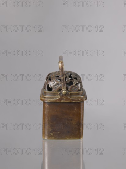 Hand warmer teaburi with lid, Japanese; Meiji period 1868–1912, 19th–20th century; bronze; rectangular form; decorated with landscapes and clouds; vessel/container; height 13.6 cm, width 10.9 cm, depth 8.2 cm., A small metal container with a rectangular body and an ornate perforated domed lid; the object shows a patinated surface in shades of brown, bronze, and hints of gold, with a curved handle rising from the lid and decorative cut-out patterns on the dome, resting on a reflective surface against a pale gray background.